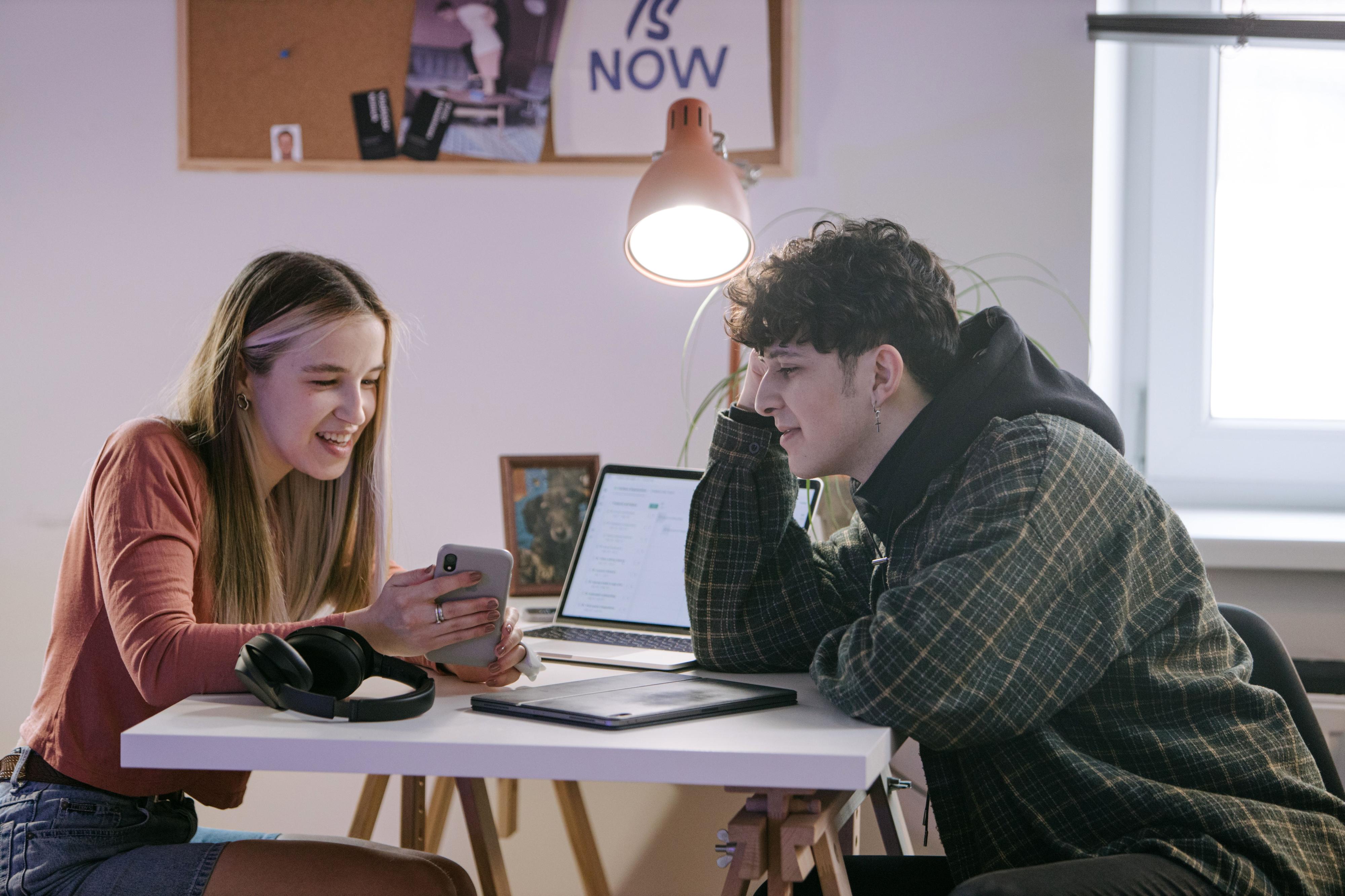 Due studenti che chiacchierano mentre usano uno smartphone in uno spazio interno comune. 